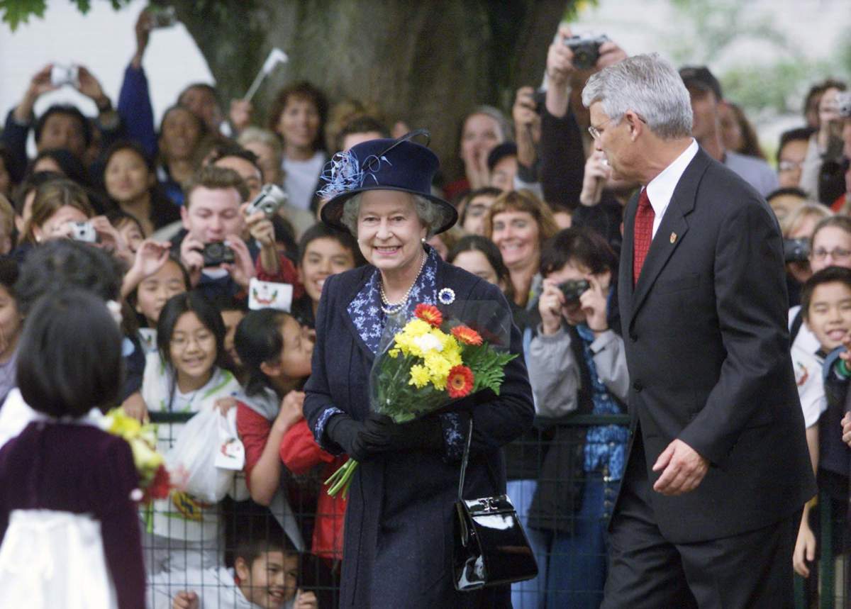 Queen Elizabeth II smiles as she is greeted by thousands of people at the University of British Columbia in Vancouver on Monday, Oct. 7, 2002. B.C. Premier Gordon Campbell guides her along her walkabout where onlookers try to get a glimpse of her. (CP PHOTO/Chuck Stoody)
