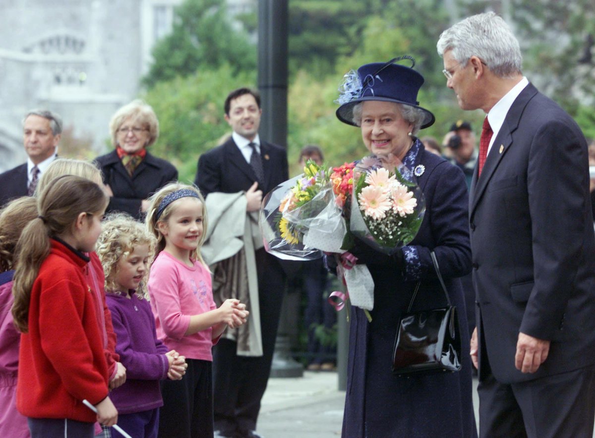 The Queen smiles after receiving flowers from school children at the University of British Columbia in Vancouver, B.C. on Monday, Oct. 7, 2002. Accompanying her is B.C. Premier Gordon Campbell.