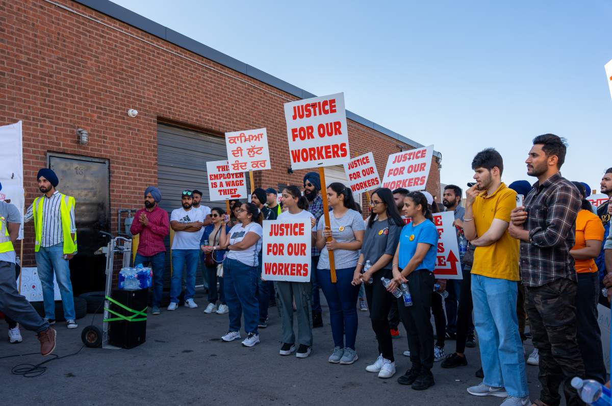 Naujawan Support Network holds a sign reading “justice for our workers” in both Punjabi and Urdu at a protest in front of Sukh Auto.