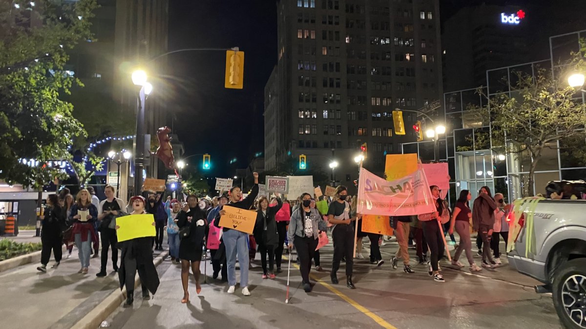 Survivors of sexual violence and supporters march through the streets of downtown Hamilton at night, holding signs and chanting.