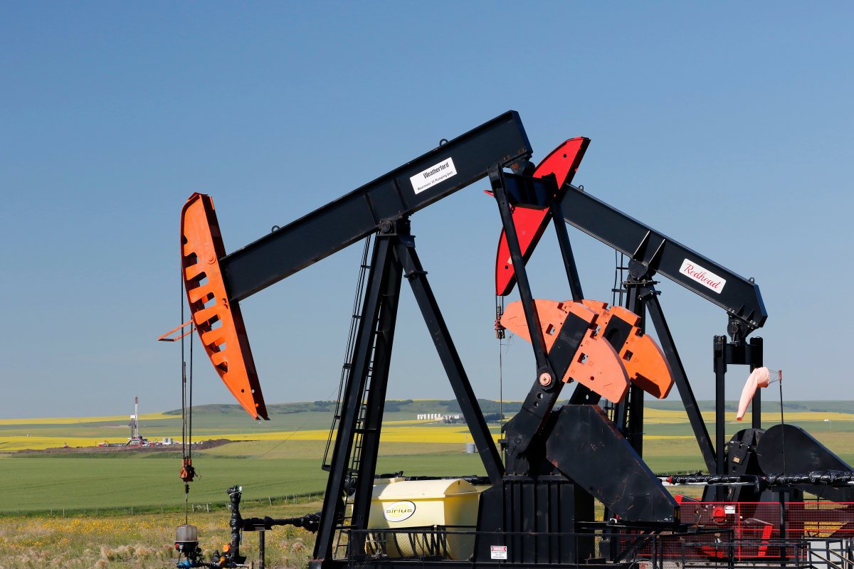 Two oilfield pumpjacks, belonging to Artis Exploration Ltd., work producing crude oil as a drilling rig, surrounded by blooming canola fields, works on a new well near Three Hills, Alberta on July 21, 2022.