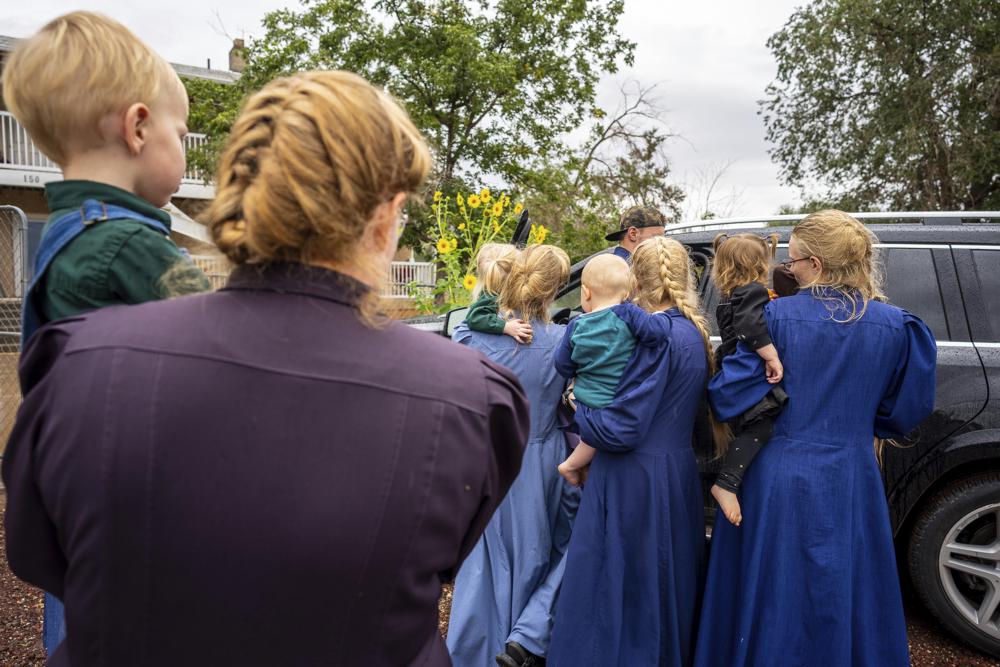 Girls in blue dresses surround a police vehicle. One girl is carrying a young child.