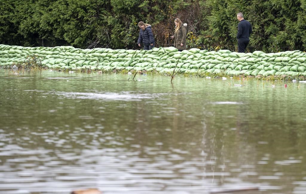 People watch the rising flood waters crossing the Canada/United States border in Huntington Village in Abbotsford, B.C., Monday, Nov. 29, 2021. The British Columbia government says it's ready to deploy sand bags and tiger dams in case flooding follows the ongoing drought. THE CANADIAN PRESS/Jonathan Hayward.