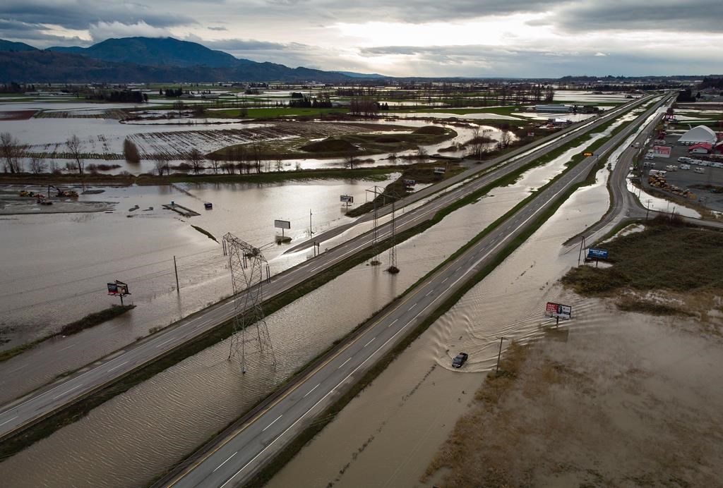 A motorist drives on a service road along the closed Trans-Canada Highway as floodwaters fill the ditches beside the highway and farmland in Abbotsford, B.C., on Wednesday, Dec. 1, 2021.