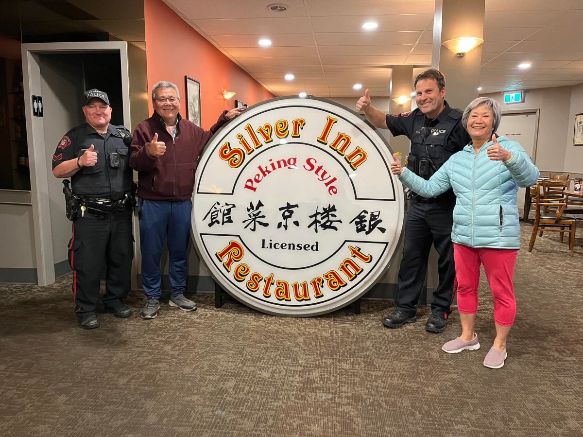 The owners of Calgary's Silver Inn Restaurant pose for a photo with Calgary police after its sign was recovered from it being stolen on Oct. 11, 2022.