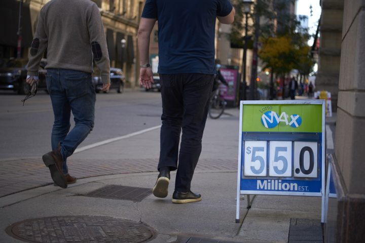 People walk past a sign for Lotto Max’s 55 million dollar draw, Toronto, Oct. 19, 2021. THE CANADIAN PRESS IMAGES/Rachel Verbin.