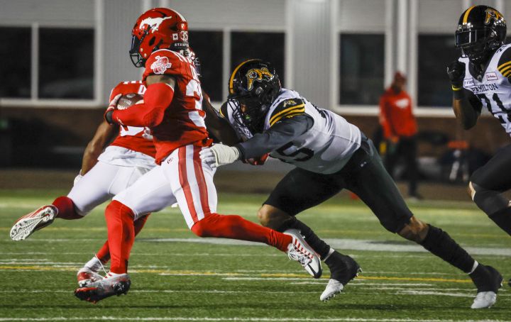 Hamilton Tiger-Cats Jovan Santos-Knox, right, grabs for Calgary Stampeders running back Ka’Deem Carey during first half CFL football action in Calgary, Friday, Oct. 14, 2022.