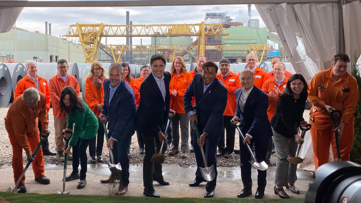 Dofasco workers join politicians in front of the steelmaker's plant, with everyone holding shovels and smiling at the camera.