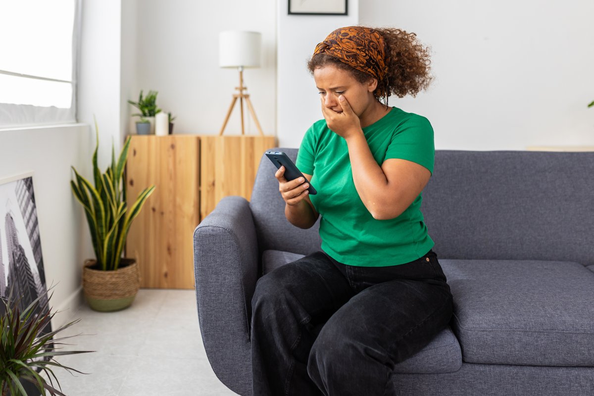 Upset confused young african woman with hand in mouth holding mobile phone receiving bad news - Frustrated millennial female checking smartphone at home