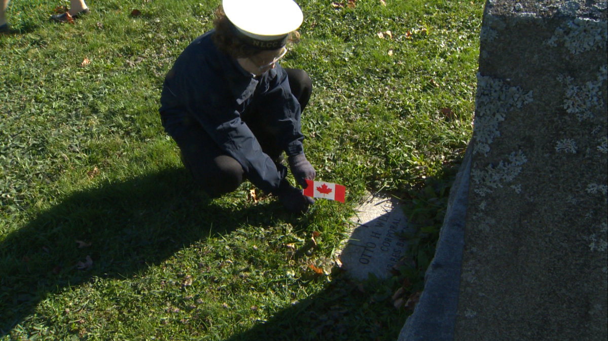 A cadet lays a flag next to a headstone