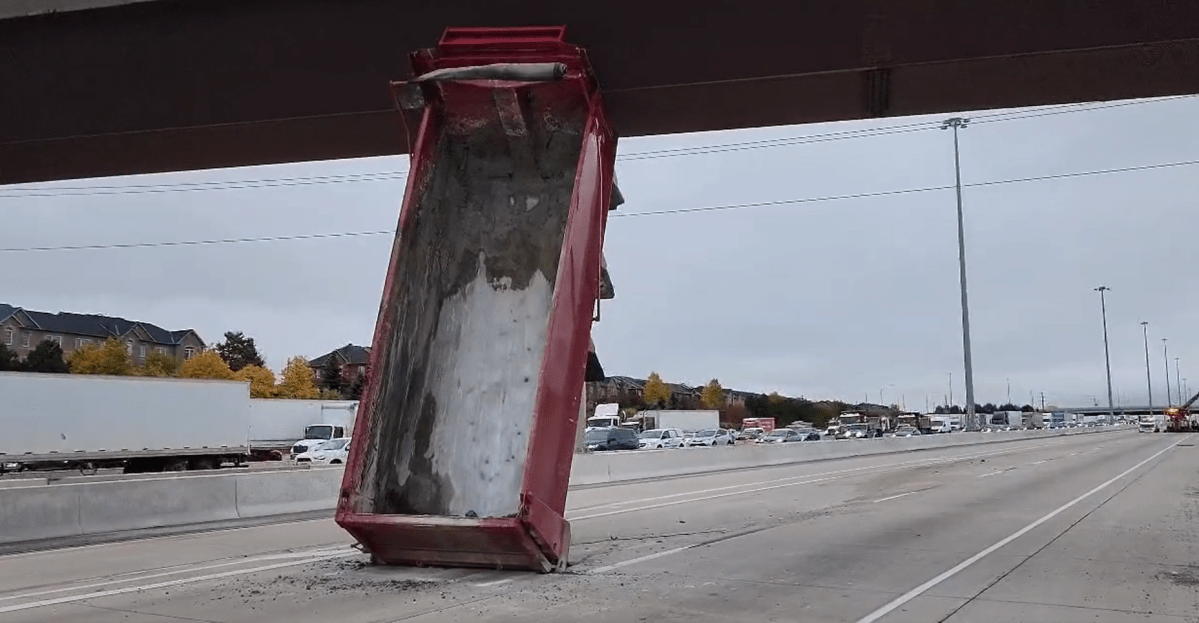 A screenshot of a video posted to Twitter by Ontario Provincial Police shows a dump truck box stuck underneath a pedestrian bridge along Highway 401.