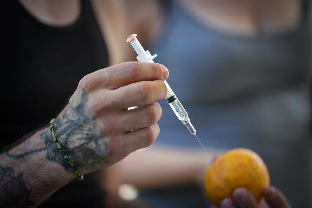 A person holds a syringe and an orange while learning how to administer Naloxone to an overdose victim, during an International Overdose Awareness Day gathering in Surrey, B.C., on Wednesday, Aug. 31, 2022.