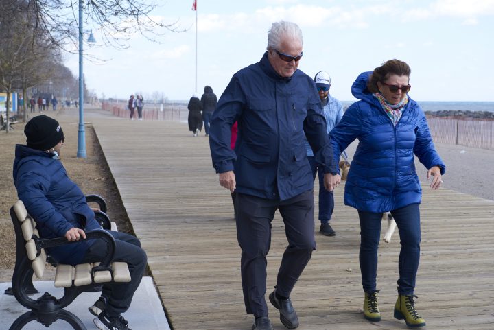 People walk at the beach on an unseasonably warm but extremely windy day, in Toronto on March 6, 2022. 