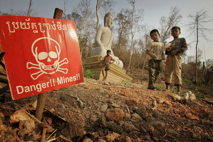 Children play near a landmine warning and a Buddhist shrine in New Village Border, Cambodia