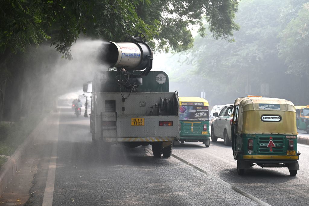 Commuters ride past an anti-smog gun spraying water to curb air pollution amid heavy smog conditions in New Delhi on November 4, 2022.