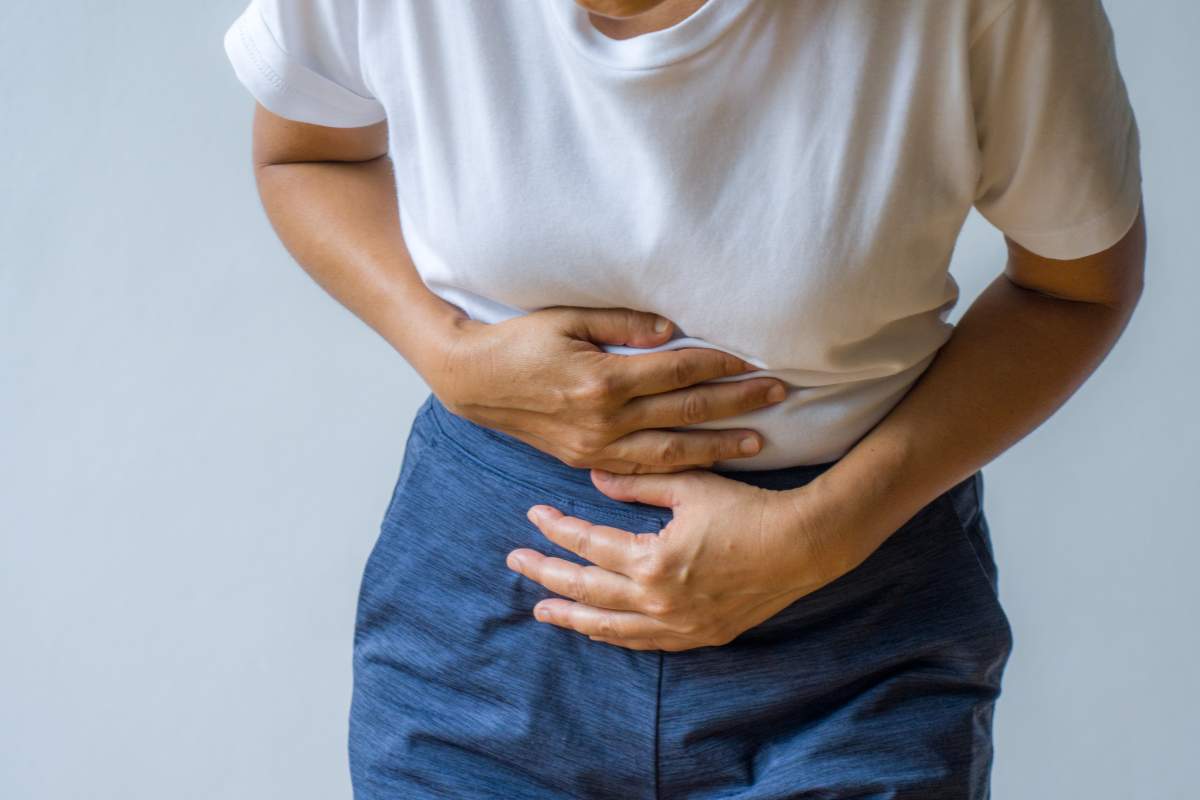 A woman in a white tee and jeans clutches her stomach.