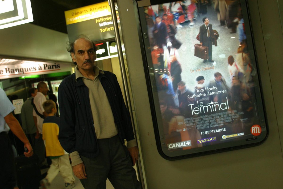 Mehran Karimi Nasseri stands beside an advertisement for the movie 'The Terminal.' `