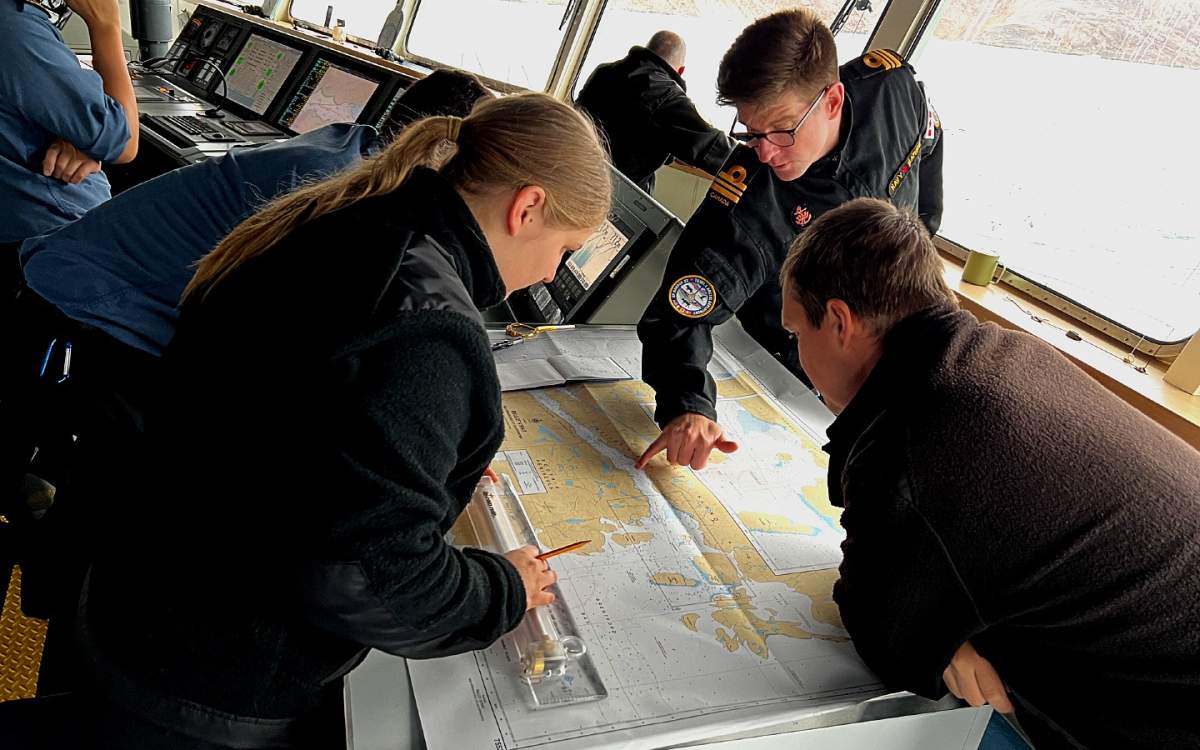 HMCS Margaret Brooke crew members gather around a map on the bridge of the ship as they navigate the Bellot Strait.