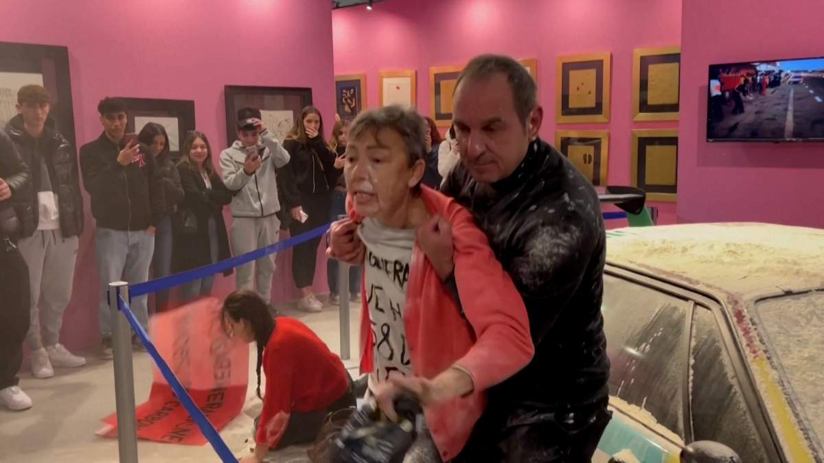 A Ultima Generazione protestor being held by a man in front of the painted Andy Warhol car.