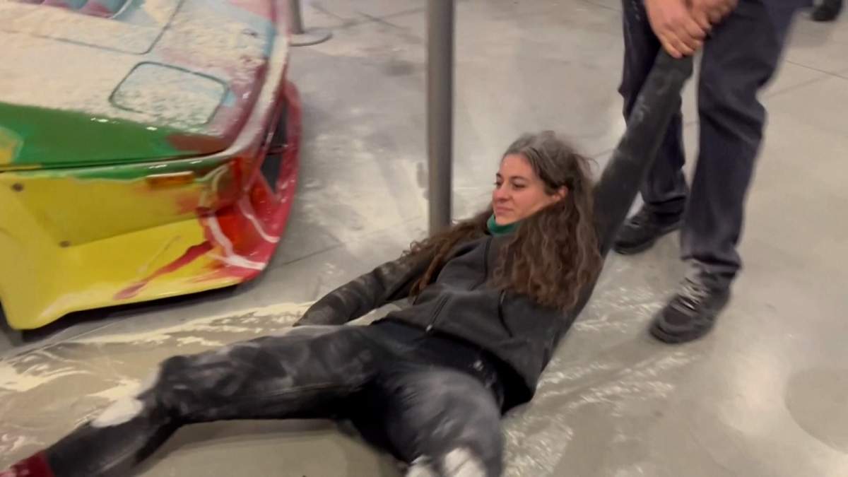 A protestor in a black sweater is dragged across a flour-covered floor.