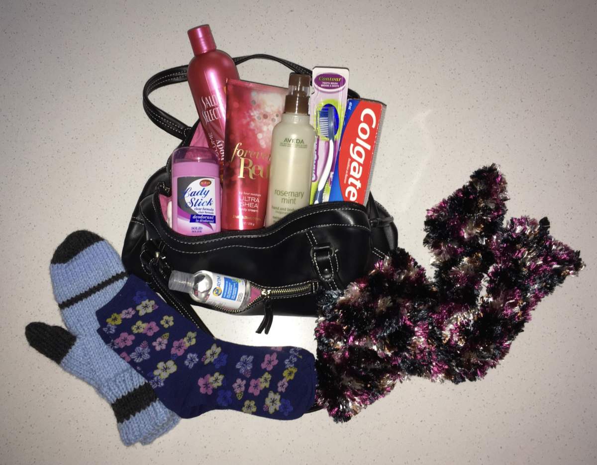 A purse full of various care products like toothpaste, deodorant, shampoo, and a toothbrush, as well as socks, mittens, and a scarf.
