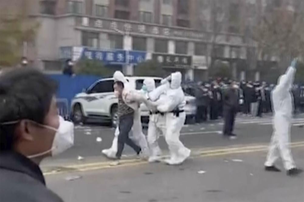 In this photo provided Nov 23, 2022, security personnel in protective clothing were seen taking away a person during protest at the factory compound operated by Foxconn Technology Group who runs the world's biggest Apple iPhone factory in Zhengzhou in central China's Henan province.
