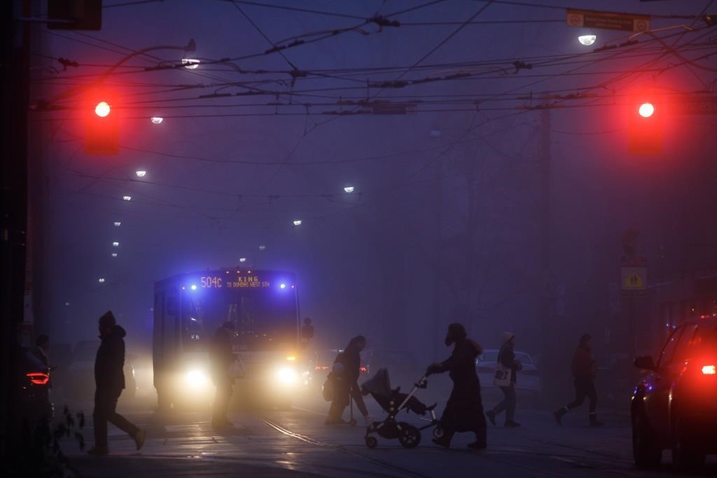 People walk through the headlights of vehicles in the evening fog in Toronto, Thursday, Nov. 24, 2022.