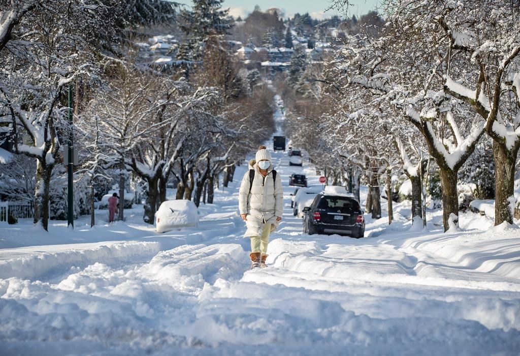 A woman bundled up for the cold weather walks up a snow-covered street in Vancouver, on Thursday, December 30, 2021. THE CANADIAN PRESS/Darryl Dyck.