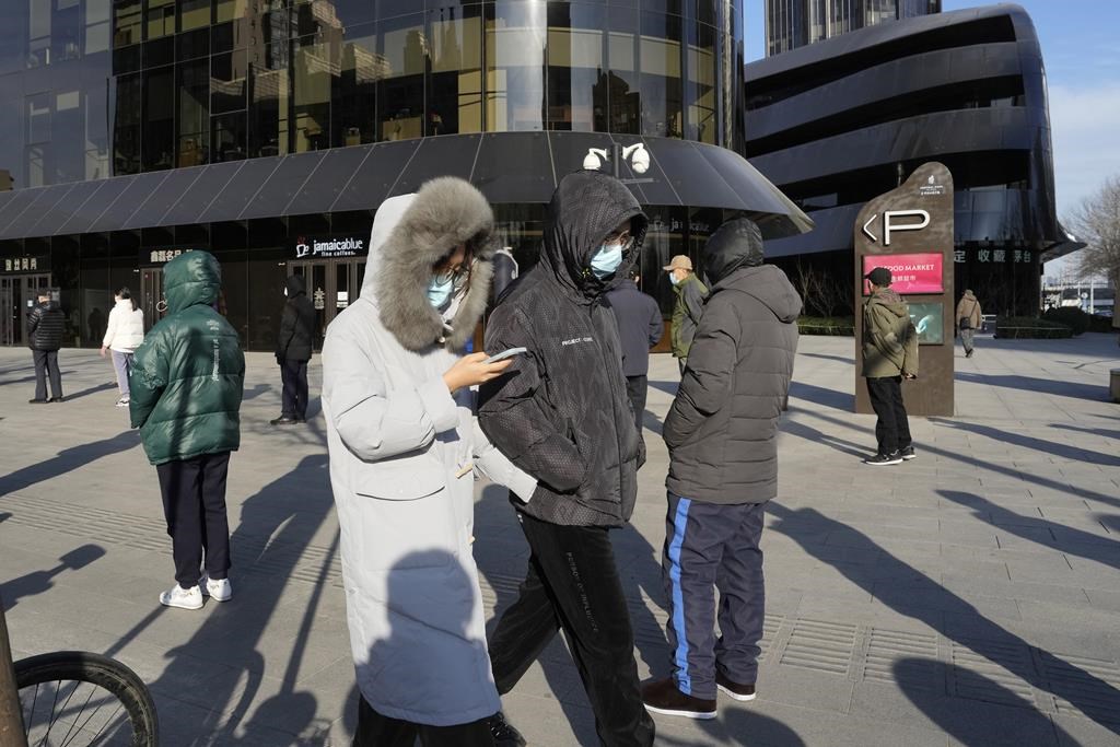 Residents wearing masks walk past others in line for COVID tests in Beijing, Wednesday, Dec. 7, 2022.