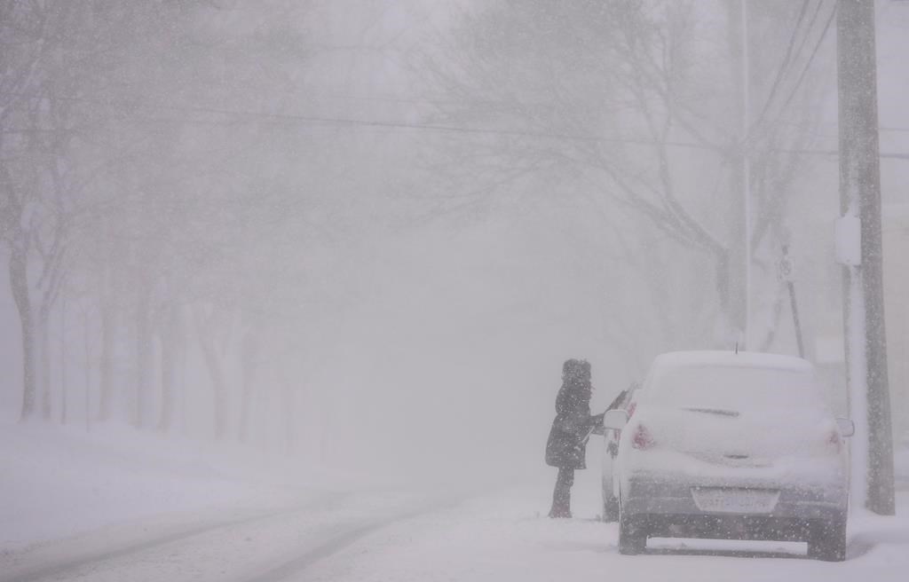 In this file photo a woman cleans snow off her car as a storm brings white-out conditions to Halifax on Thursday, March 8, 2018. Winter storm warning remain in effect for much of the Maritimes as a snowstorm has forced the closure of schools in parts of Nova Scotia and P.E.I. .