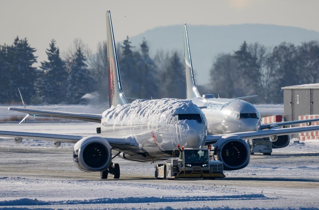 An Air Canada aircraft covered with snow and ice is moved by a tug as a WestJet aircraft is seen being moved behind it at Vancouver International Airport in Richmond, B.C., on Wednesday, Dec. 21, 2022.