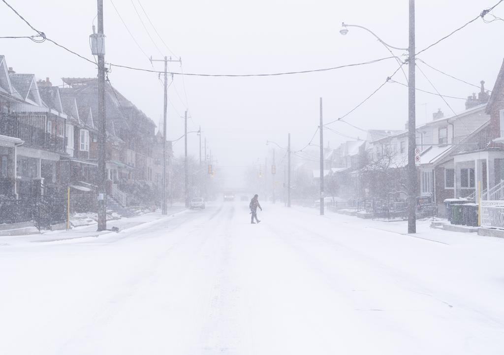 A man crosses a road during a snowstorm in Toronto on Friday, December, 23, 2022. A winter storm warning is in place for most of southern Ontario. 