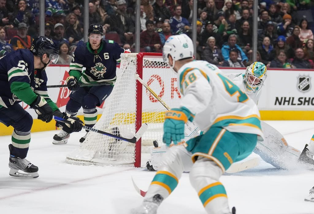 Vancouver Canucks' Bo Horvat, left, scores against San Jose Sharks goalie James Reimer, back right, during the first period of an NHL hockey game in Vancouver, on Tuesday, Dec. 27, 2022.