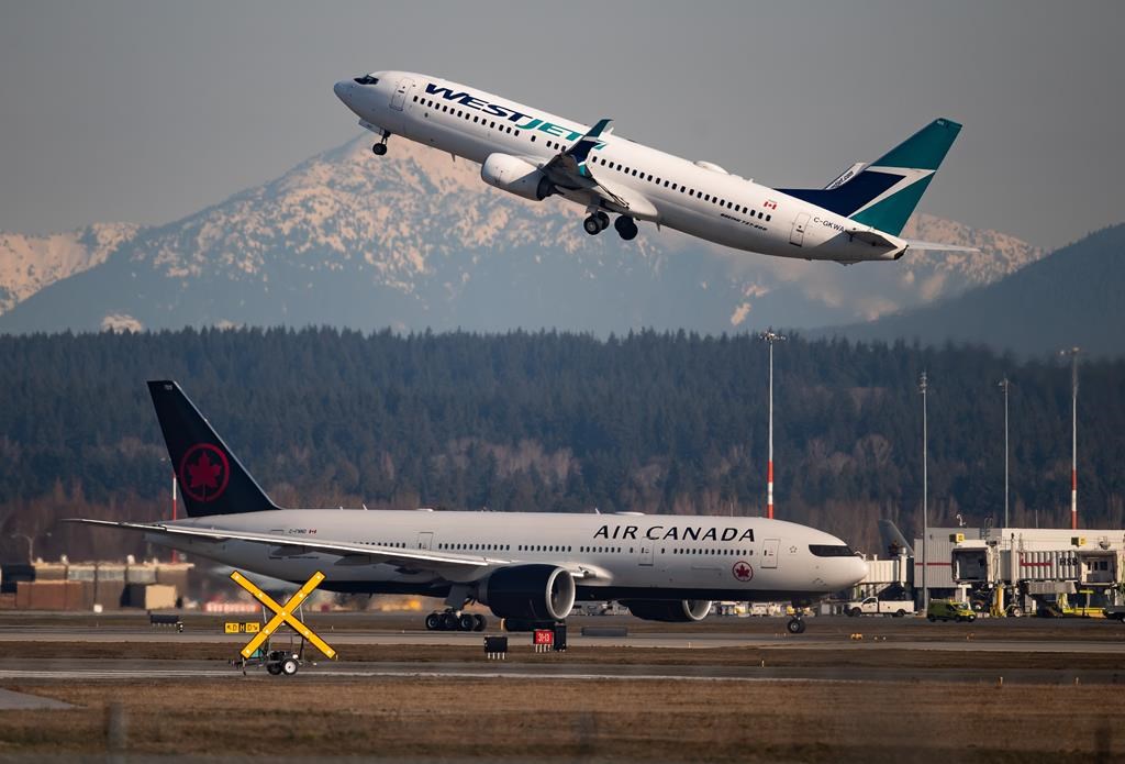 An Air Canada flight taxis to a runway as a WestJet flight takes off at Vancouver International Airport, in Richmond, B.C., on March 20, 2020. A Calgary woman is frustrated after a WestJet customer service scam tried to swindle her money and banking information. THE CANADIAN PRESS/Darryl Dyck.