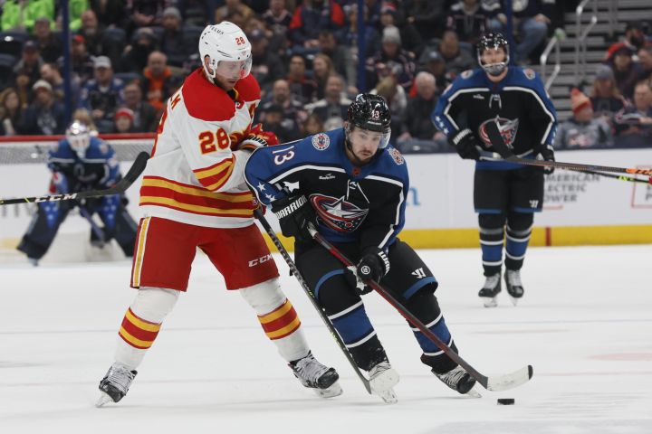 Columbus Blue Jackets’ Johnny Gaudreau, right, carries the puck across the blue line past Calgary Flames’ Elias Lindholm during the second period of an NHL hockey game Friday, Dec. 9, 2022, in Columbus, Ohio.