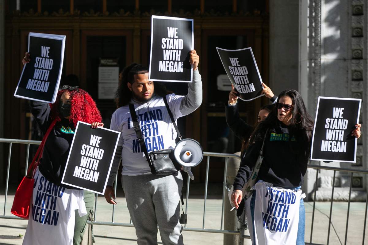 A group of people holding "We stand with Megan" signage and T-shirts.