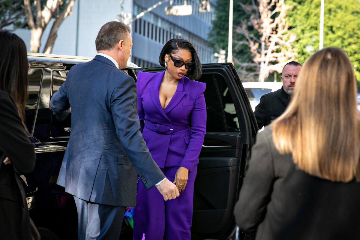Megan Thee Stallion leaves a black vehicle dressed in a purple suit and sunglasses.