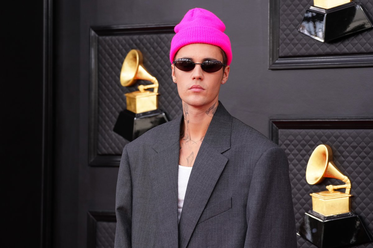 Justin Bieber in a pink beanie and sunglasses. He is wearing a suit jacket.