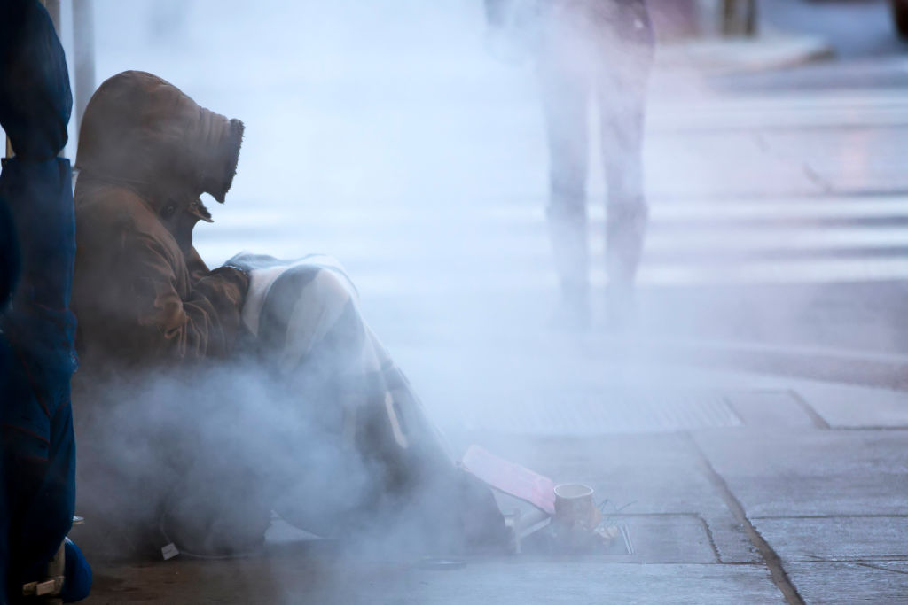 FILE PHOTO - A man tries to keep warm near a steam vent in downtown Toronto, Ontario.