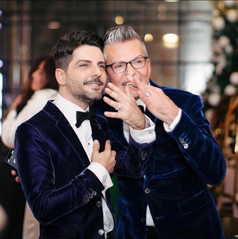 Randy Fenoli and Mete Kobal flash their new silver engagement rings to the camera. They are wearing blue suede suits.