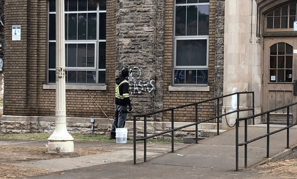 A worker cleans anti-mask graffiti off of the outside of Westdale Secondary School.