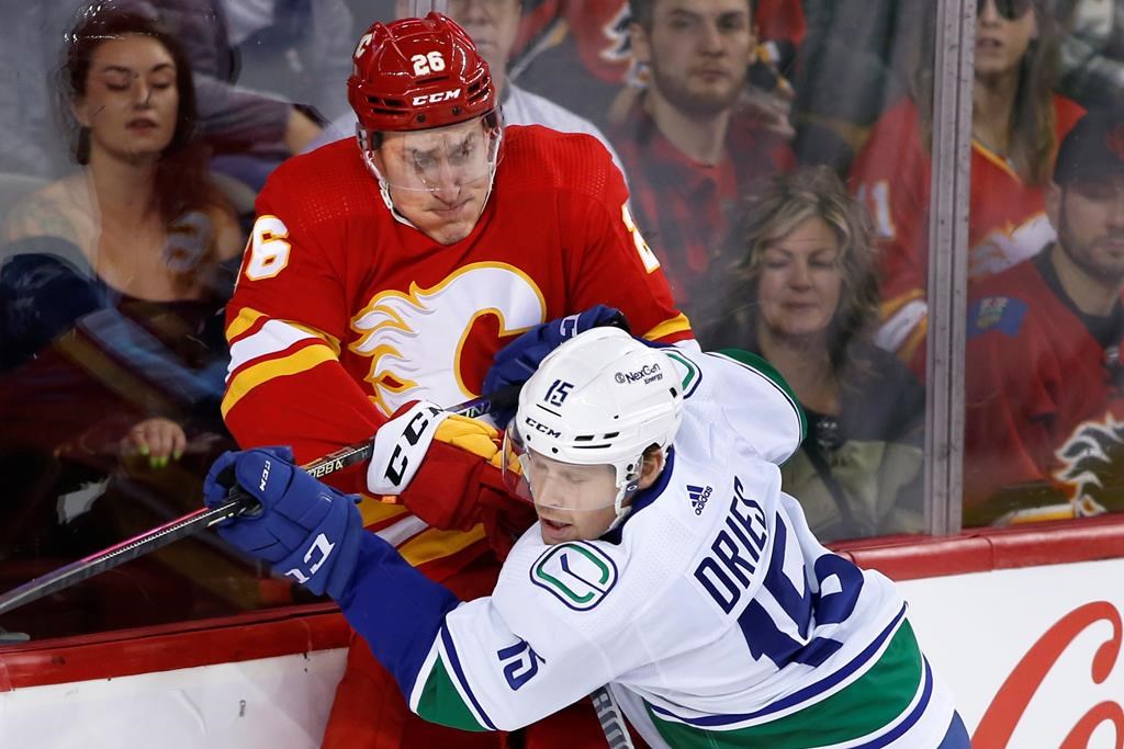Vancouver Canucks' Sheldon Dries, right, hits Calgary Flames' Michael Stone during first period NHL hockey action in Calgary, Alta., Saturday, Dec. 31, 2022. THE CANADIAN PRESS/Larry MacDougal.