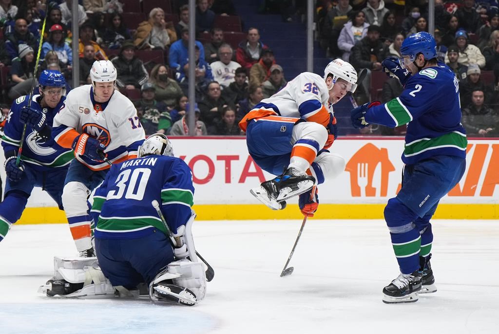 New York Islanders' Ross Johnston (32) jumps out of the way to avoid being hit by the puck as Vancouver Canucks goalie Spencer Martin (30) makes the save while Luke Schenn (2), Travis Dermott (24) and New York's Matt Martin (17) watch during the second period of an NHL hockey game in Vancouver on Tuesday, Jan. 3, 2023.