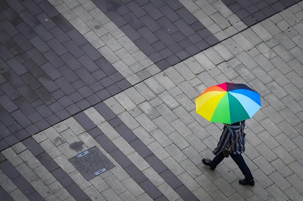A pedestrian carries an umbrella as light rain falls in Surrey, B.C., on Friday, Oct. 21, 2022.