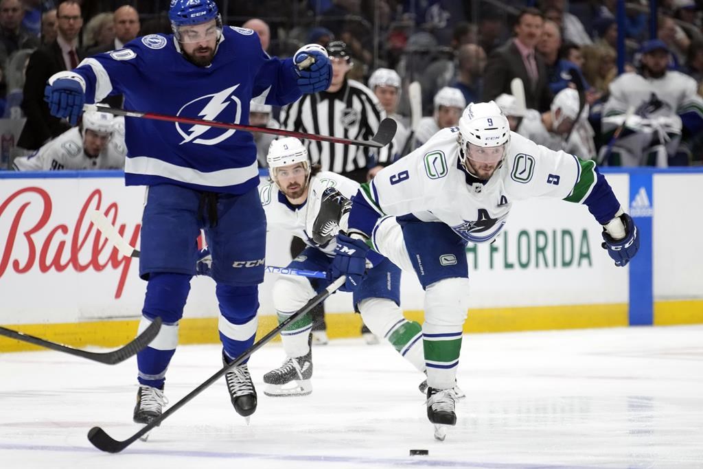 Vancouver Canucks center J.T. Miller (9) gets held by Tampa Bay Lightning left wing Nicholas Paul (20) for a penalty during the third period of an NHL hockey game Thursday, Jan. 12, 2023, in Tampa, Fla.