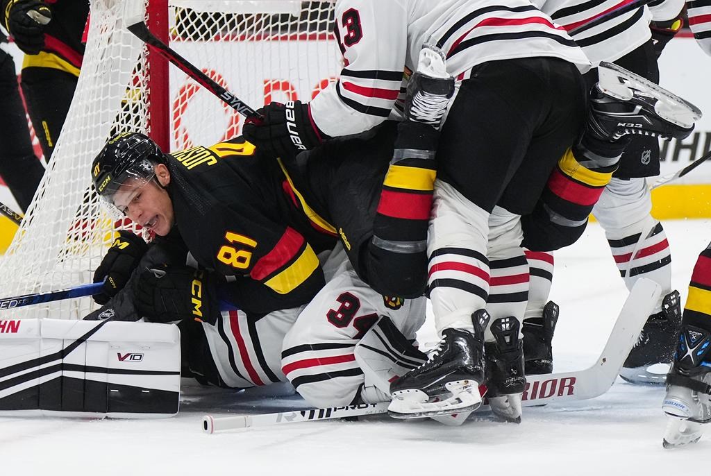 Vancouver Canucks' Dakota Joshua (81) lands on top of Chicago Blackhawks goalie Petr Mrazek (34) after being checked by Max Domi (13), after scoring a goal during the third period of an NHL hockey game in Vancouver, on Tuesday, January 24, 2023.