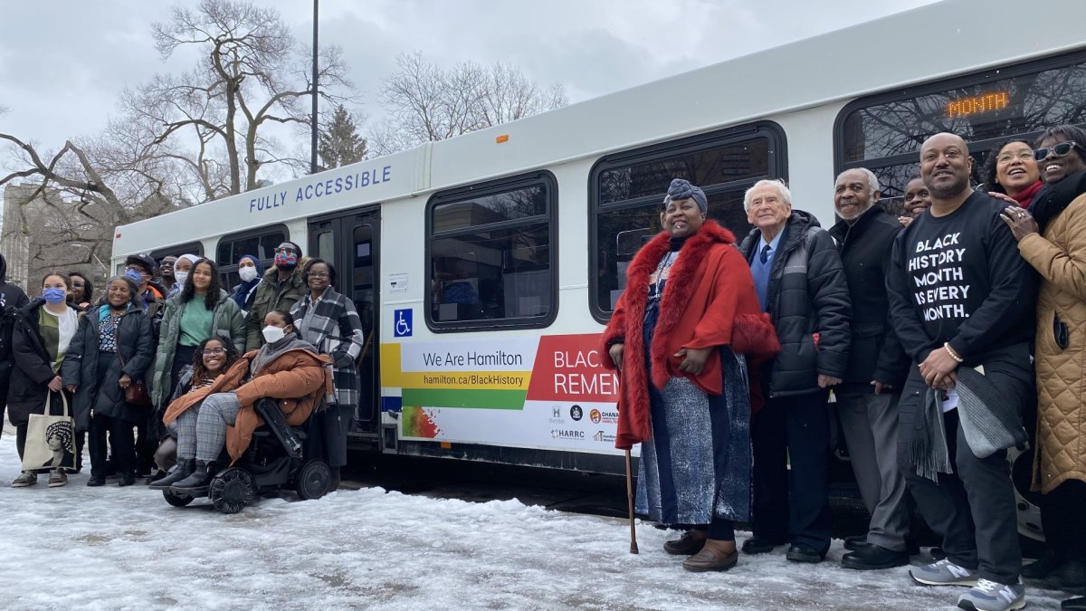 Organizers and speakers at Hamilton's "Black History Remembered" launch pose in front of an HSR bus that bears imagery related to the celebratory initiative.