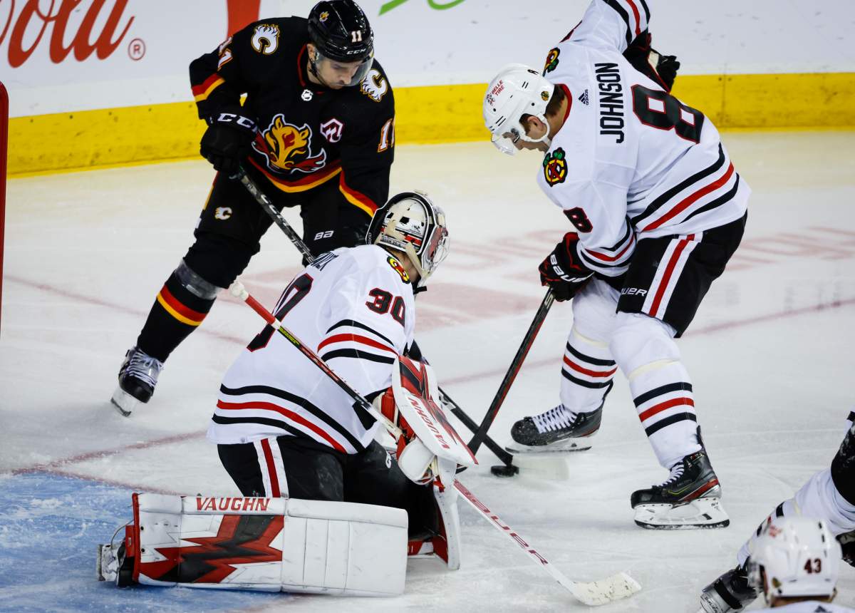 Chicago Blackhawks defenceman Jack Johnson, right, battles for the puck with Calgary Flames forward Mikael Backlund, left, as goalie Jaxson Stauber looks on during third period NHL hockey action in Calgary, Thursday, Jan. 26, 2023.