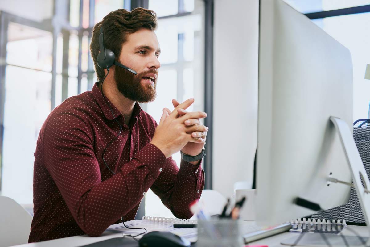 Cropped shot of a handsome young businessman sitting alone and wearing a headset while using a computer in the office
