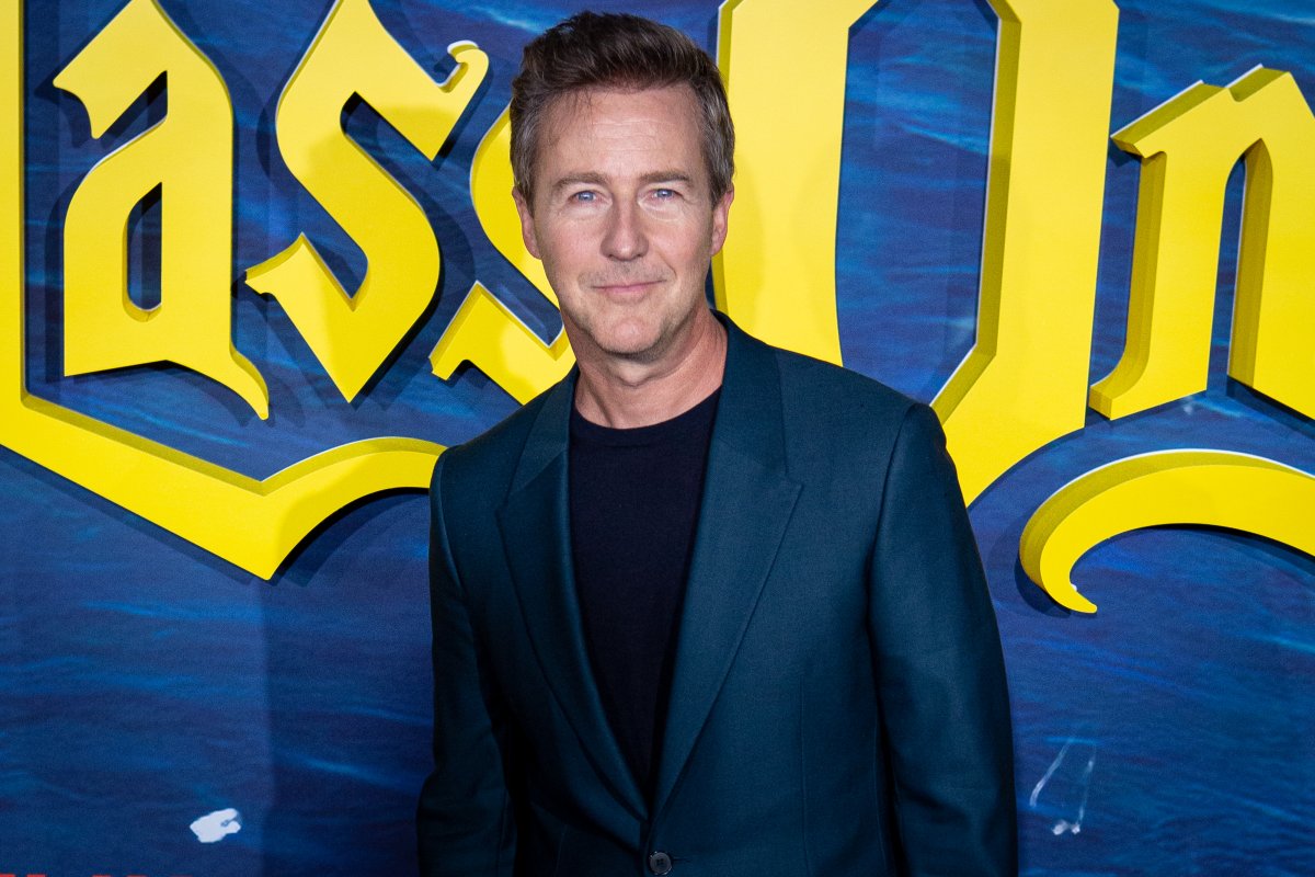Edward Norton on a red carpet. He is wearing a blue suit jacket.